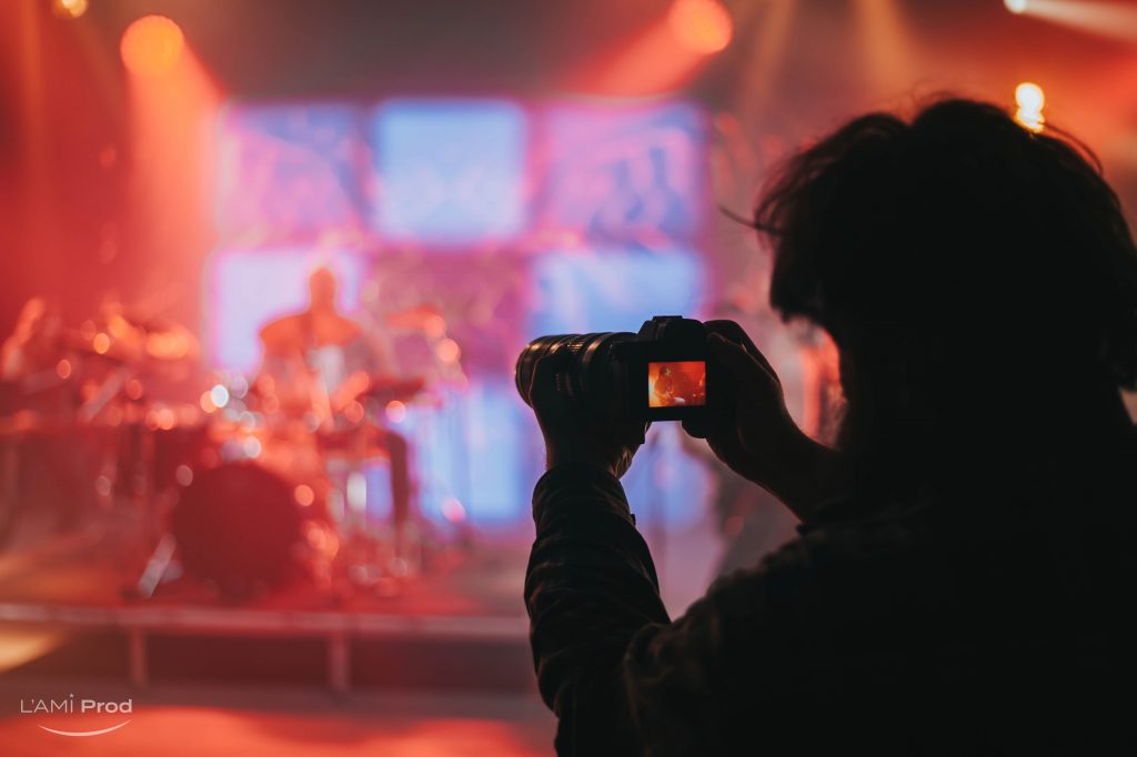 Silhouette of a photographer taking shot of a musician on the stage with the pink lights during concert on a festival