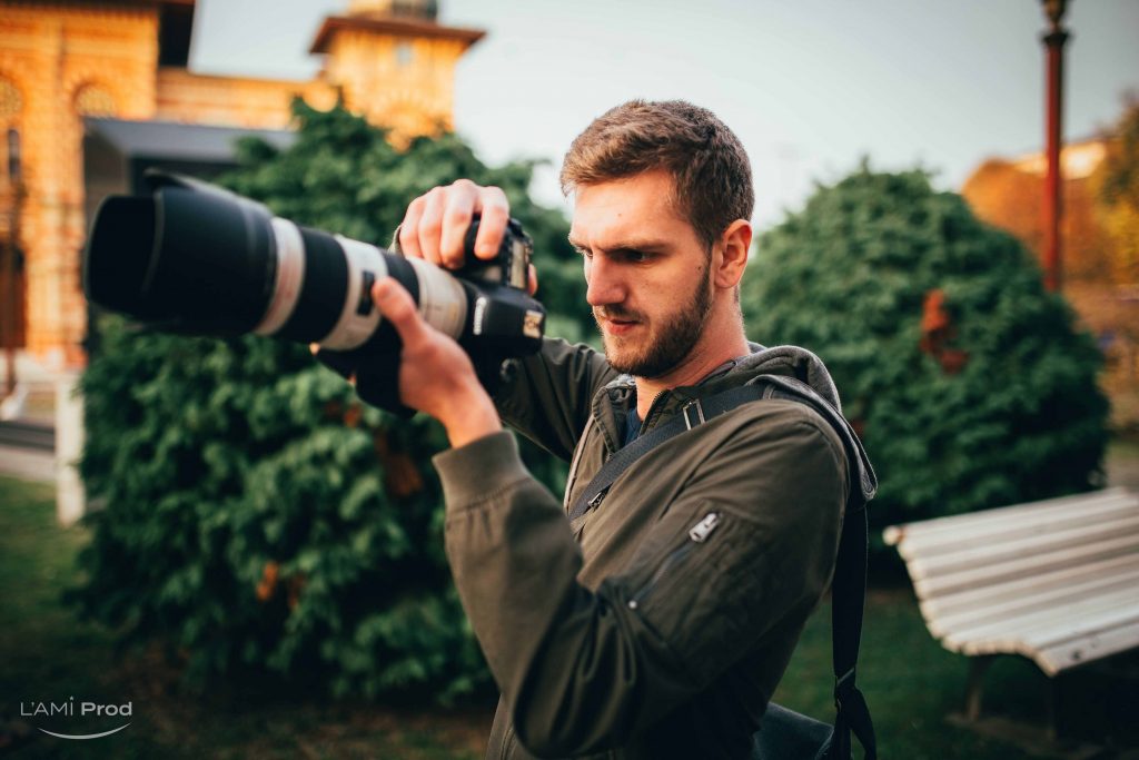 A shallow focus of a young Caucasian male photographer filming an event in a garden